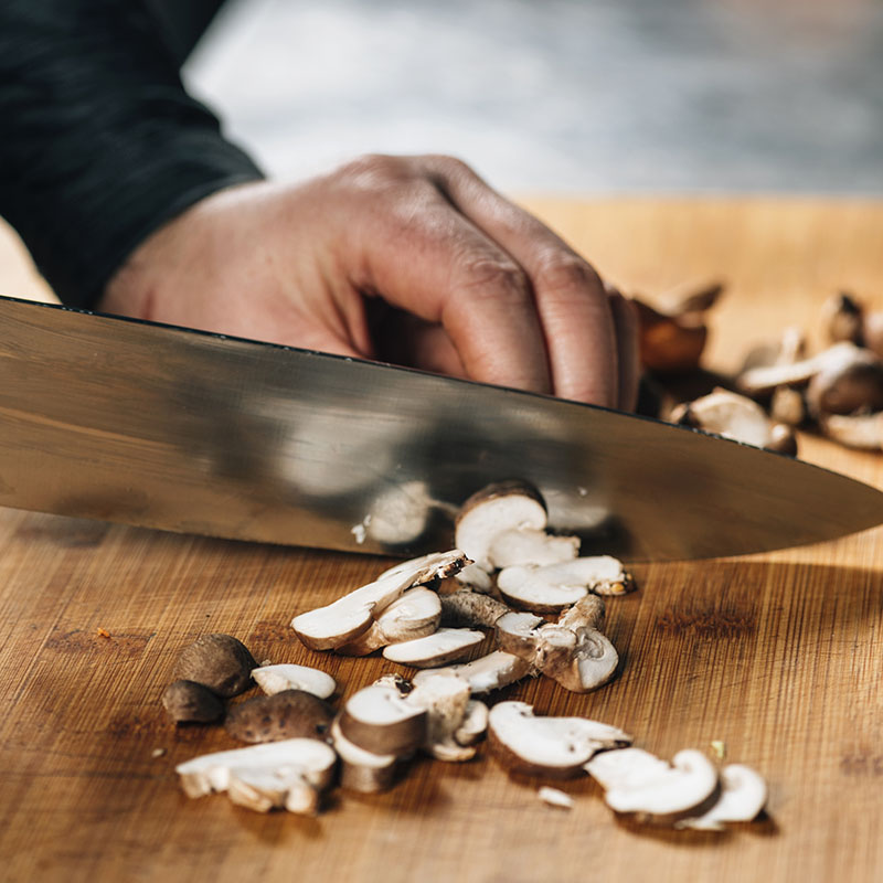 Chef cutting shiitake mushrooms with knife on a wooden cutting board